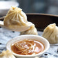 Steamed dumplings with a small bowl of soup on a wooden tray.