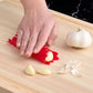 Person using a red garlic peeler on garlic cloves on a wooden cutting board.
