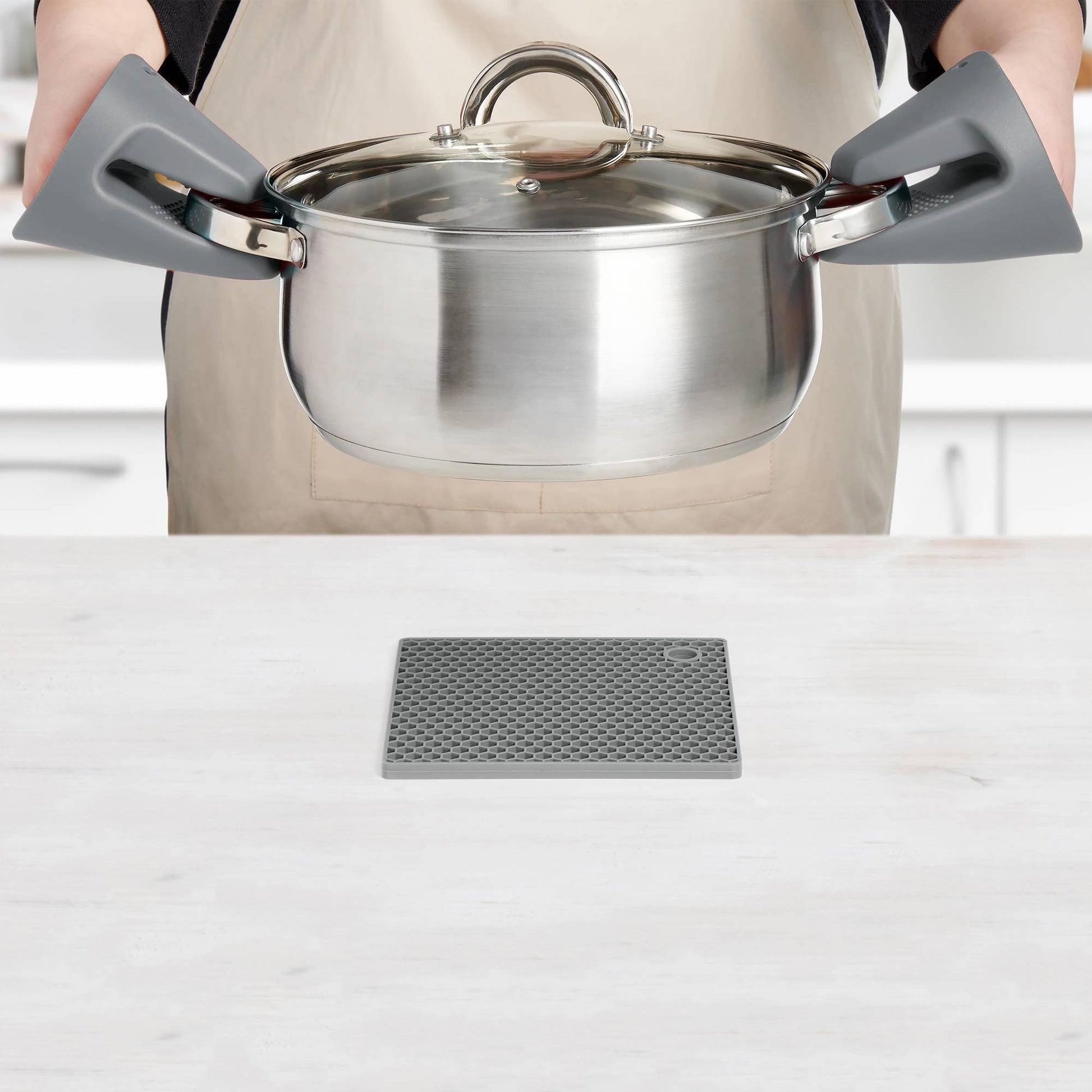 Person holding a stainless steel pot with a lid on a kitchen counter.