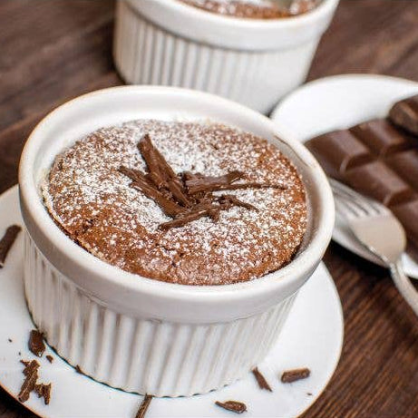 Chocolate souffle in a white ramekin with a side of chocolate bars on a wooden surface.