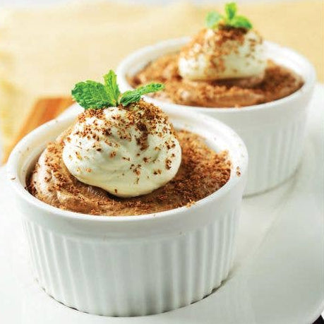 Two small desserts in white ramekins with whipped cream and a dusting of cinnamon on a light background.