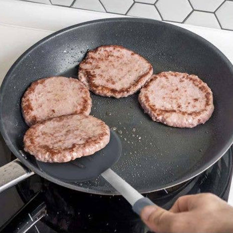 Hamburgers being cooked in a frying pan on a stove.