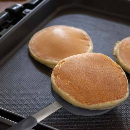 Three pancakes being cooked on a griddle with a spatula.