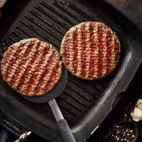 Two grilled hamburgers on a grill pan with a dark background