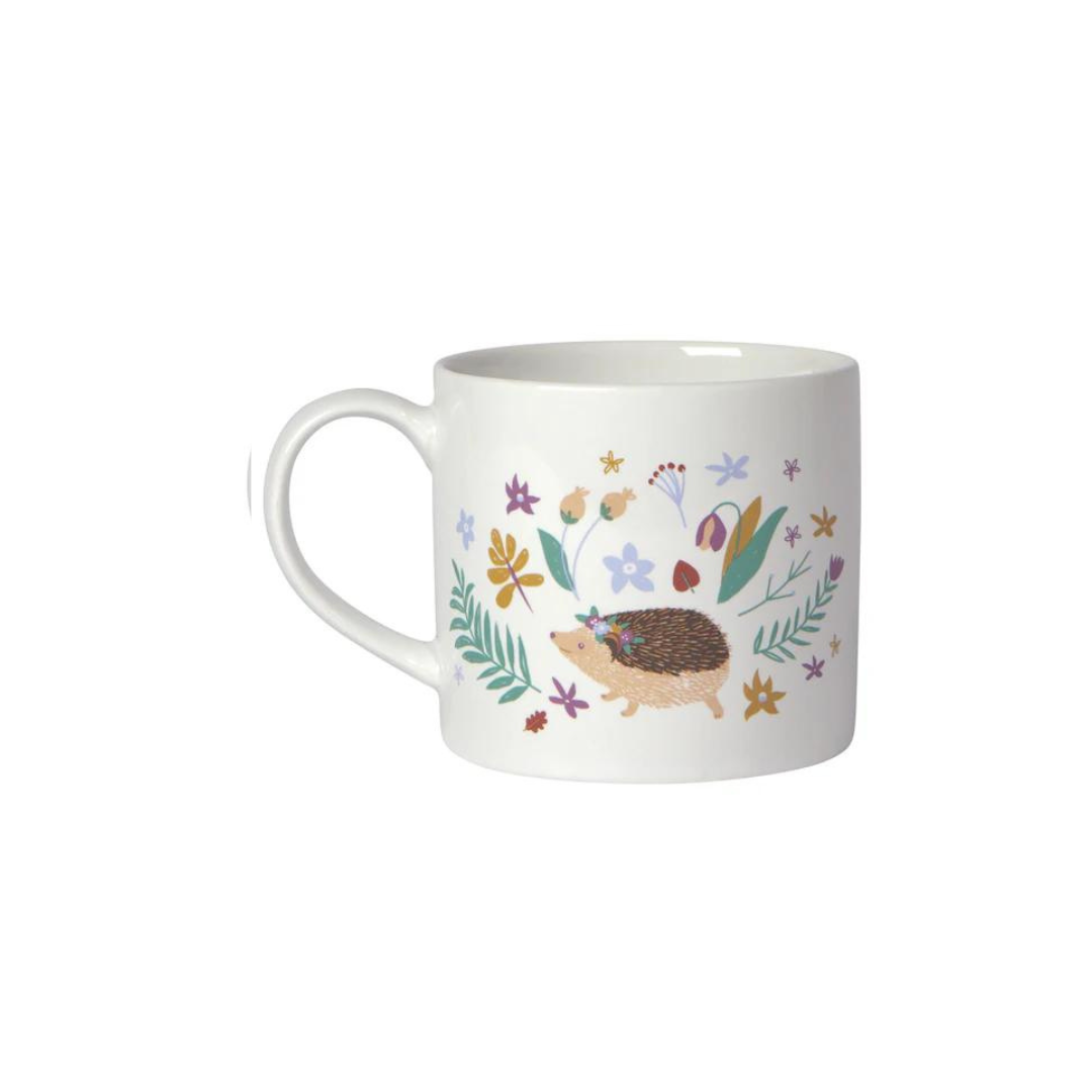  "Hedge Hugs" Mug in a Box brings a cozy, nature-inspired charm to your mornings. Featuring a whimsical hedgehog surrounded by wildflowers and a smooth white interior, 