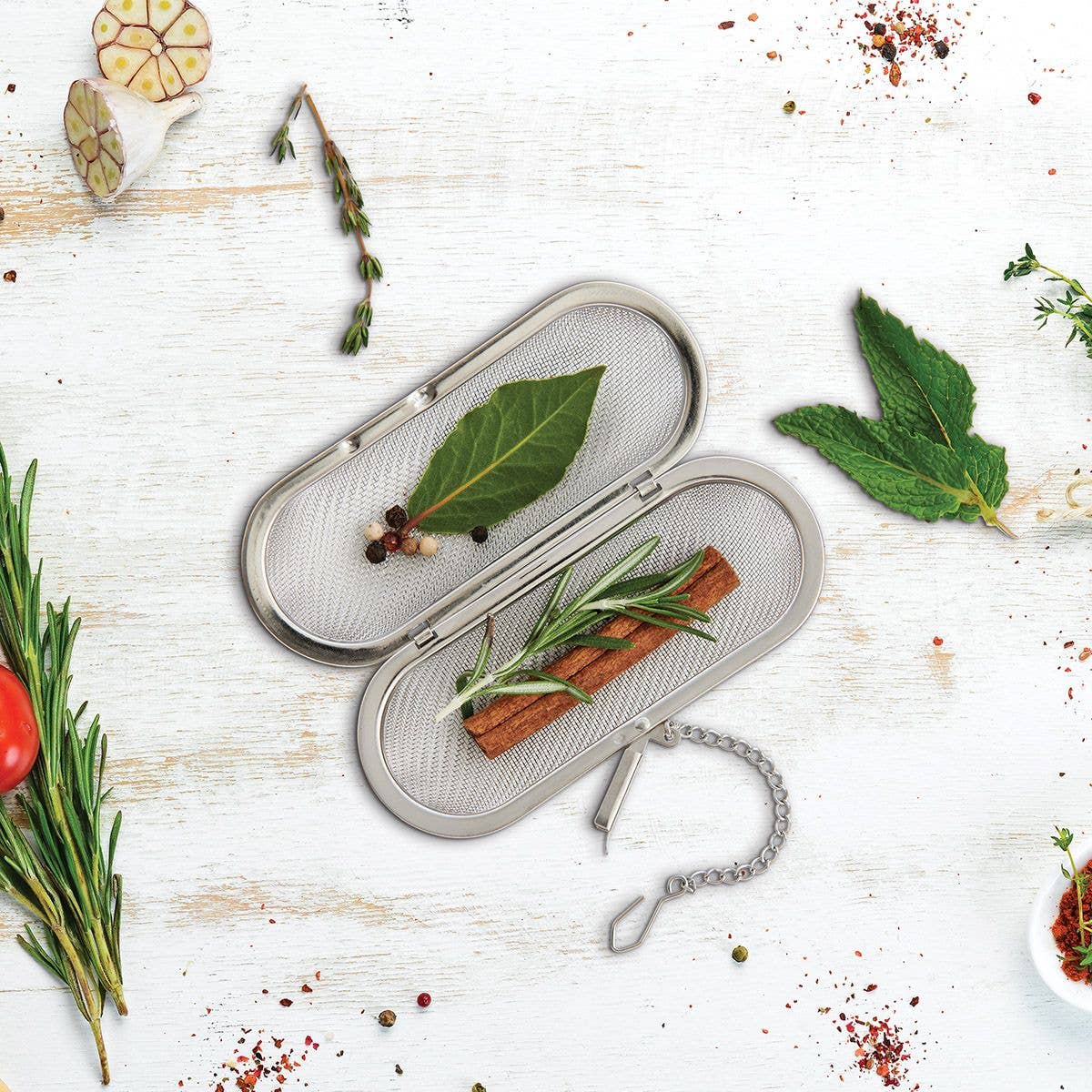 Metallic tea infuser with herbs on a white wooden surface