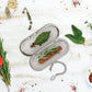 Metallic tea infuser with herbs on a white wooden surface