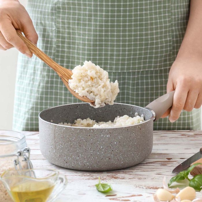 Person cooking in a gray speckled pot with a wooden spoon, wearing a green checkered apron.
