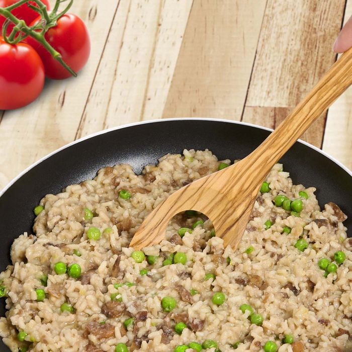 Risotto with peas in a black pan on a wooden surface with tomatoes.