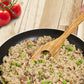 Risotto with peas in a black pan on a wooden surface with tomatoes.