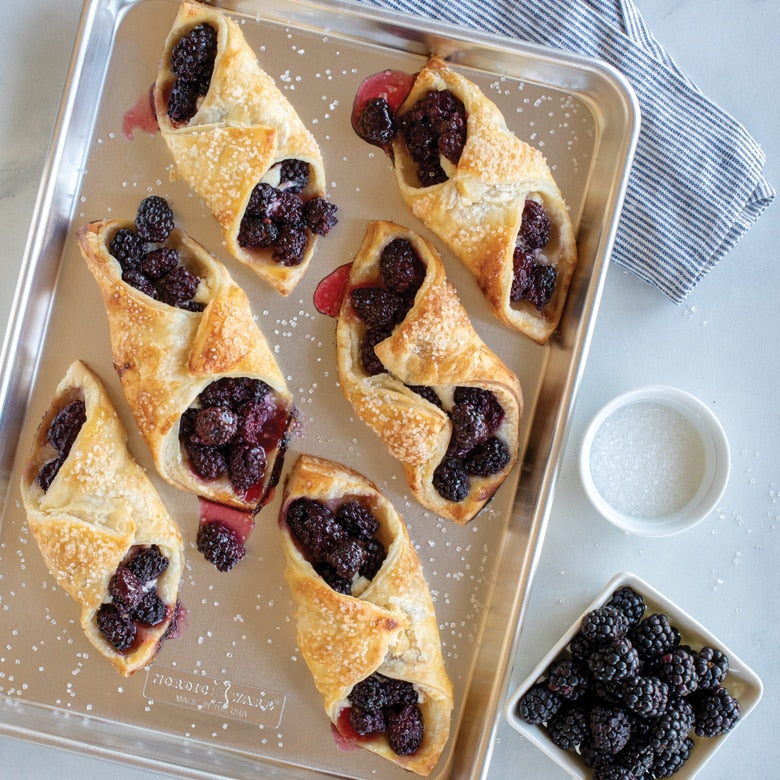 Pastry crescents with blackberries on a baking tray, with a bowl of blackberries and salt nearby.