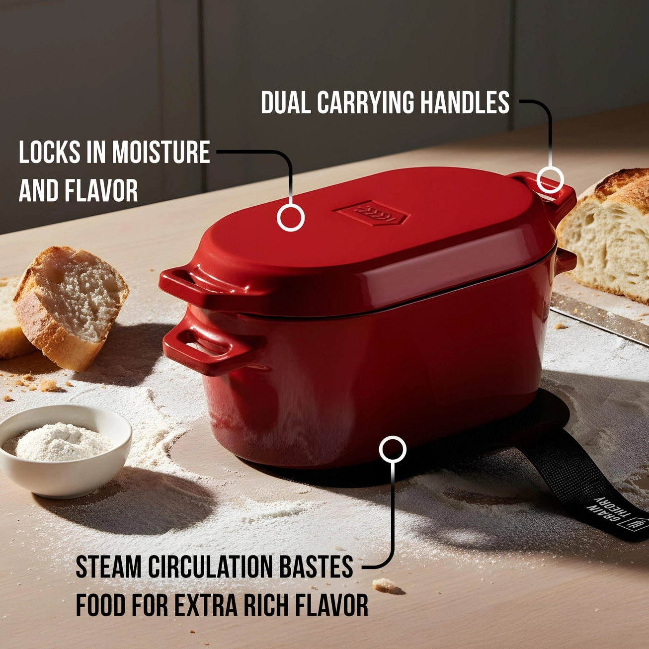 Red enameled cast iron roaster with features highlighted on a wooden surface with bread and flour.