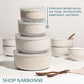 A set of Narbonne ceramic bowls and mugs with matching lids, stacked in the center. The bowls feature different geometric and textured patterns in beige and white.