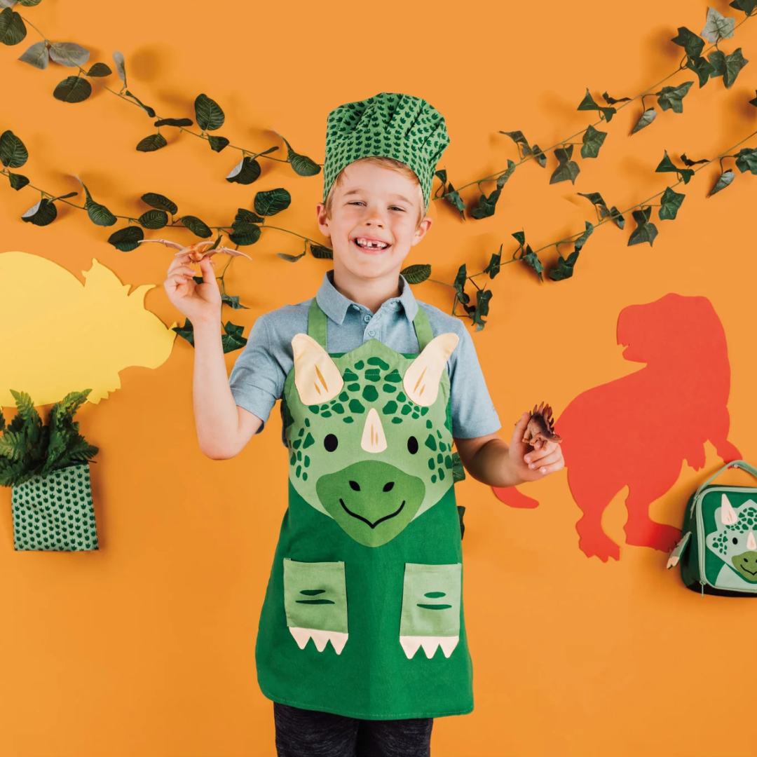 Let your little ones step into the kitchen with a smile in the Dino Apron &amp; Hat Set! Featuring an adorable green triceratops design, this set is perfect for budding chefs. The adjustable neck and waist ties ensure a comfortable and secure fit, while the matching hat adds an extra touch of fun and flair to their cooking adventures. 