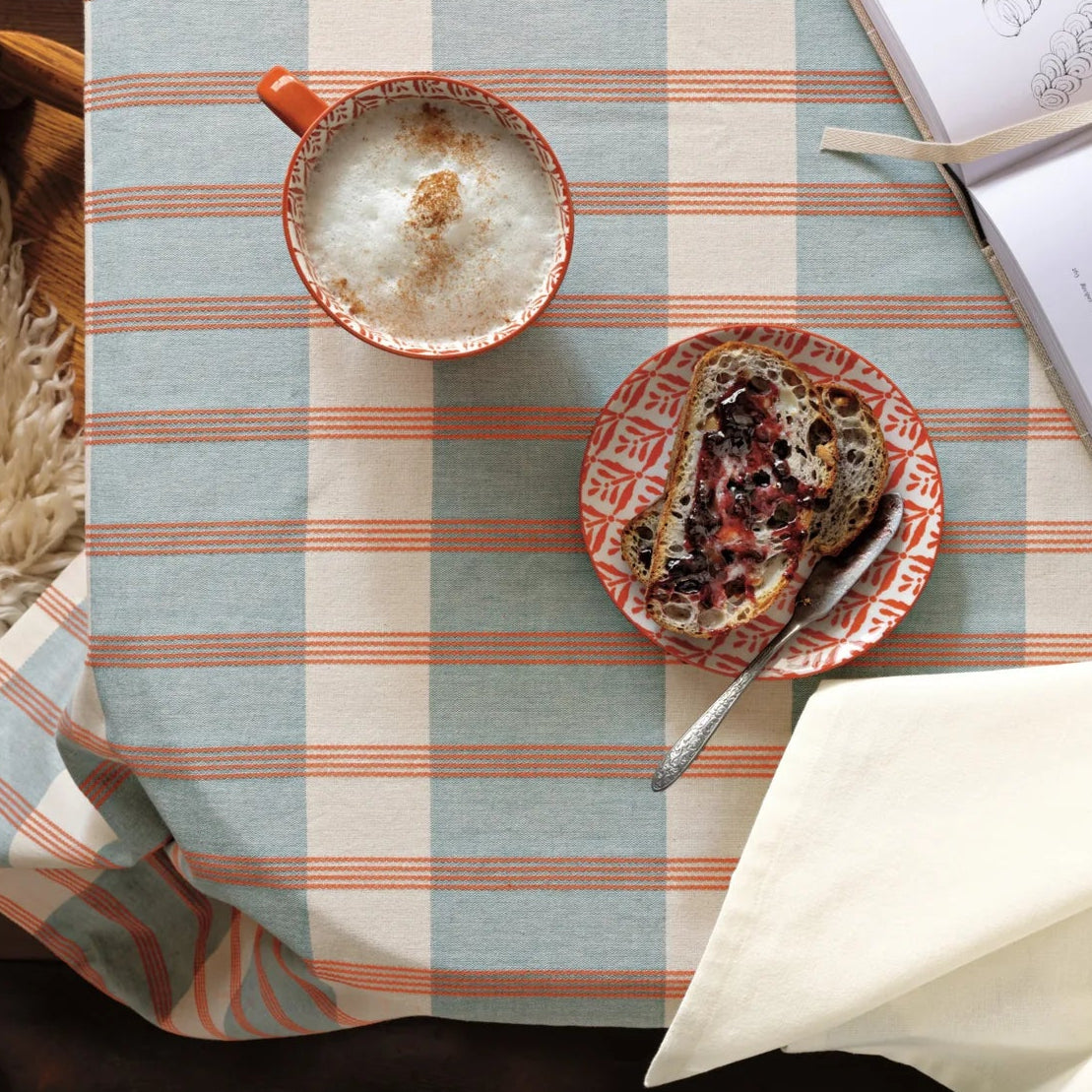 Table setting with a mug, plate of food, and book on a striped tablecloth.
