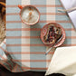 Table setting with a mug, plate of food, and book on a striped tablecloth.