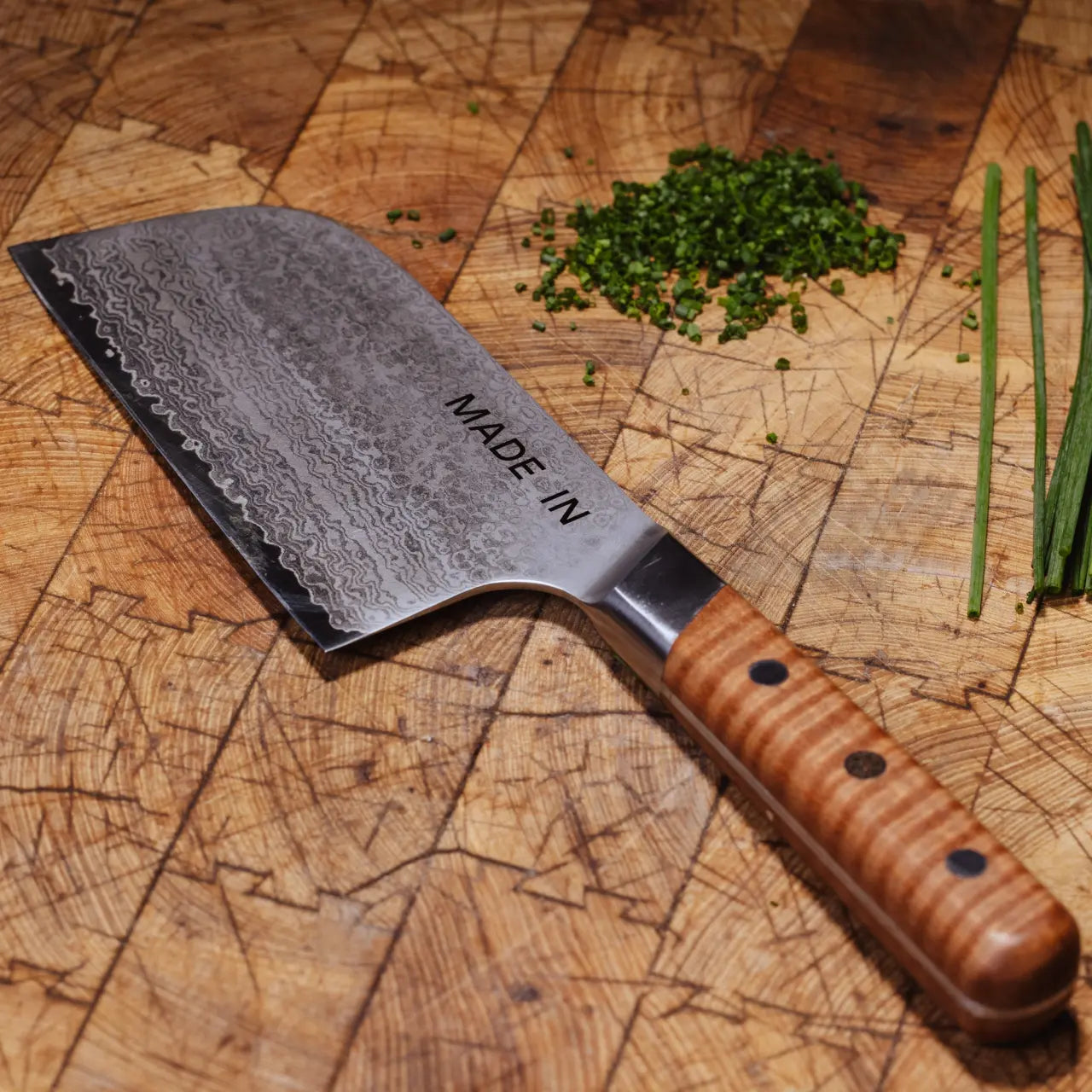 Kitchen knife with wooden handle on a wooden cutting board with chopped herbs.