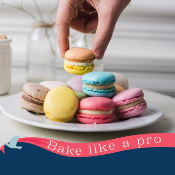 Colorful macarons on a plate with a hand picking one, set against a neutral background.