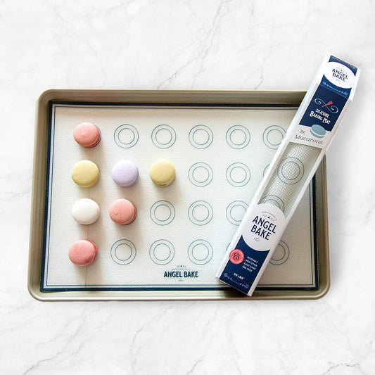 Baking sheet with macaron silicone mold and colorful macaron shells on a white surface