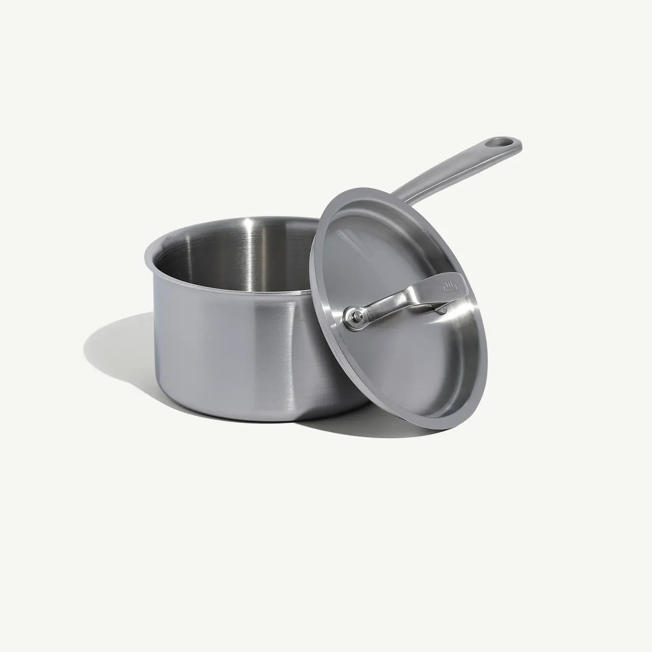 A stainless steel saucepan with a lid and a long handle, set against a white background.