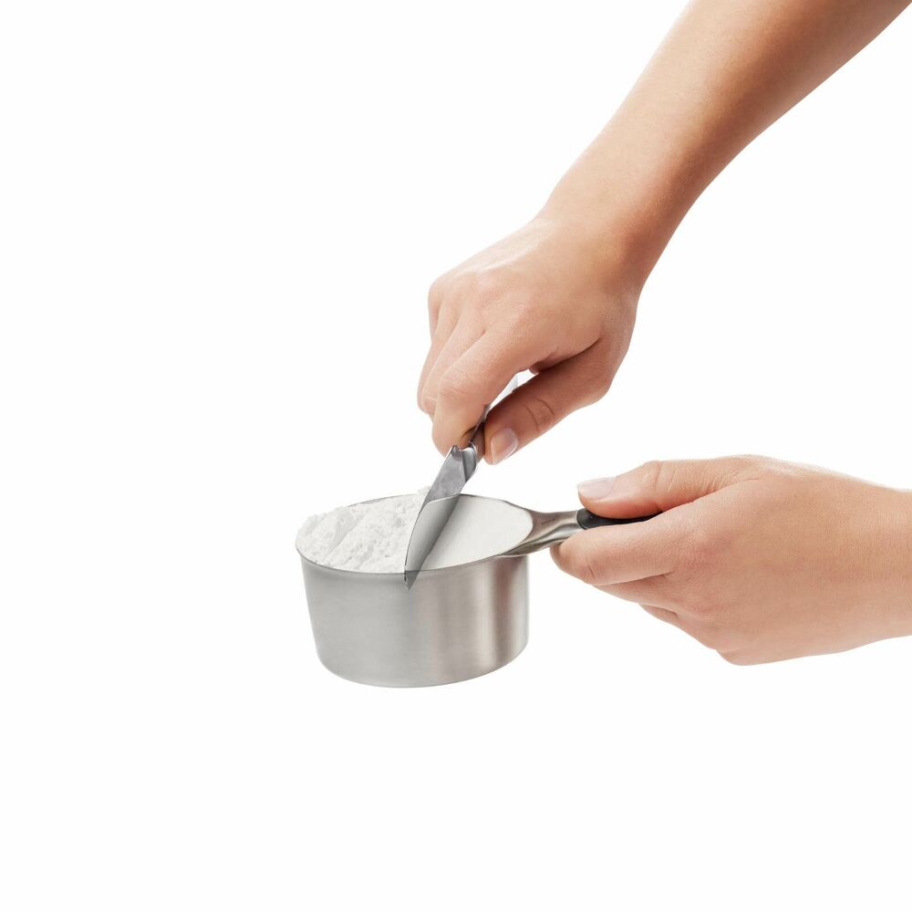 Hand using knife to even out a silver measuring cup of white powder