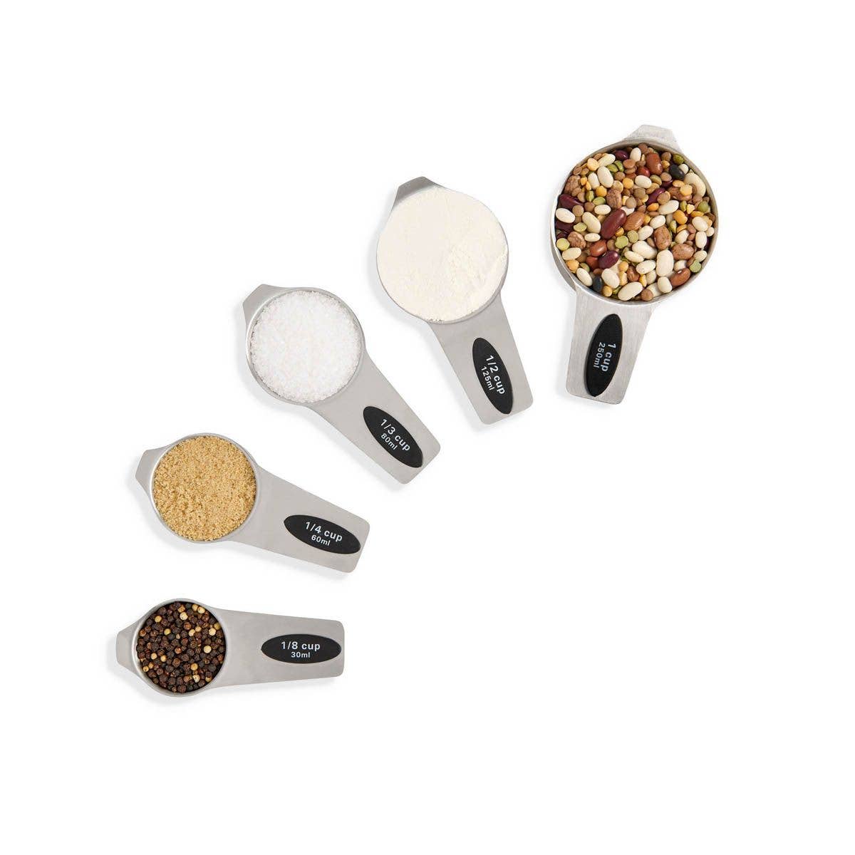 Set of five measuring spoons with different measurements filled with various substances on a white background