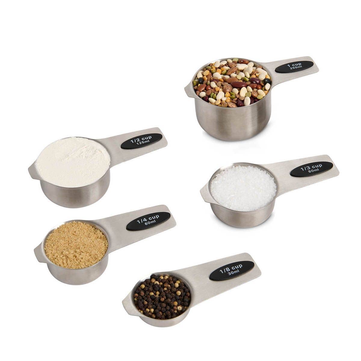 Set of stainless steel measuring cups with different measurements filled with various ingredients on a white background.