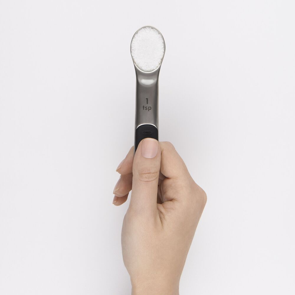 Hand holding a metal 1 tsp measuring spoon of salt