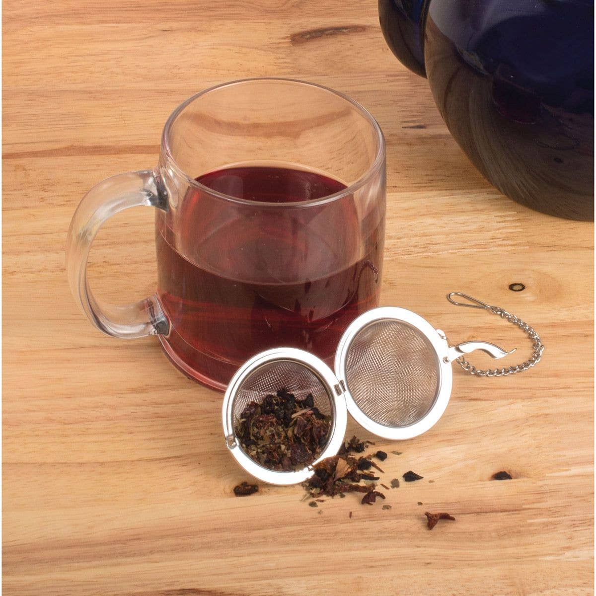 Clear mug with red tea and metal tea infuser on wooden surface