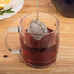 Clear glass mug with tea and metal infuser on a wooden surface