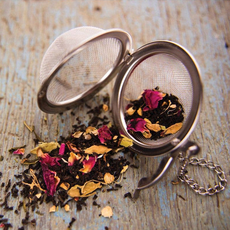 Tea infuser with dried tea leaves and flowers on a wooden surface