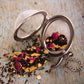 Tea infuser with dried tea leaves and flowers on a wooden surface