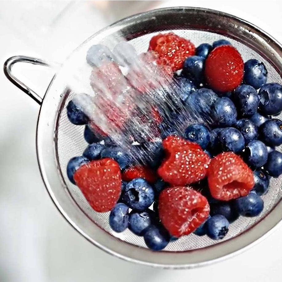 Berries being rinsed under running water in a metal strainer.