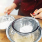 Mesh strainer being held over a metal bowl with a white powder