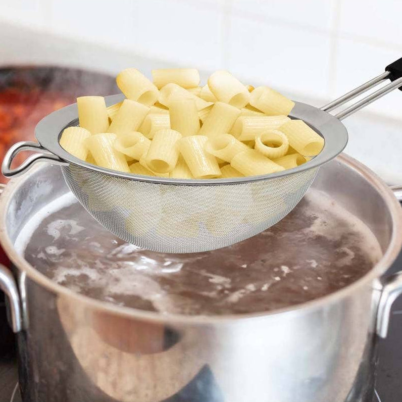 Pasta being drained from boiling water using a metal strainer.