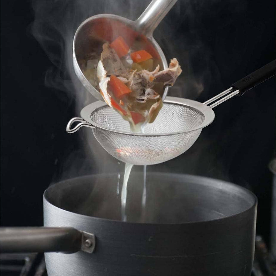Vegetable soup being ladled from a pot into a strainer over another pot on a stove.