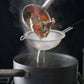 Vegetable soup being ladled from a pot into a strainer over another pot on a stove.