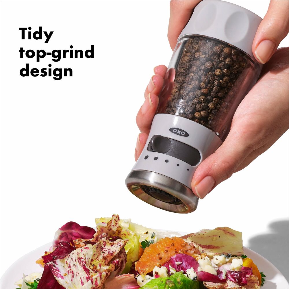 Hand using pepper grinder with tidy top grind design.