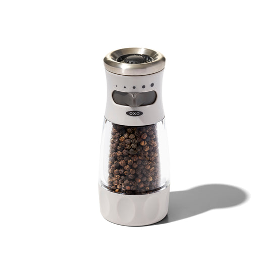 OXO pepper grinder with black peppercorns on a white background