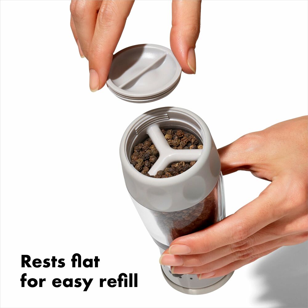 Hands holding pepper grinder showing the pepper corns rest flat for refill. 