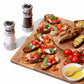 Salt and pepper grinders with cutting board and tomatoes on toast. 