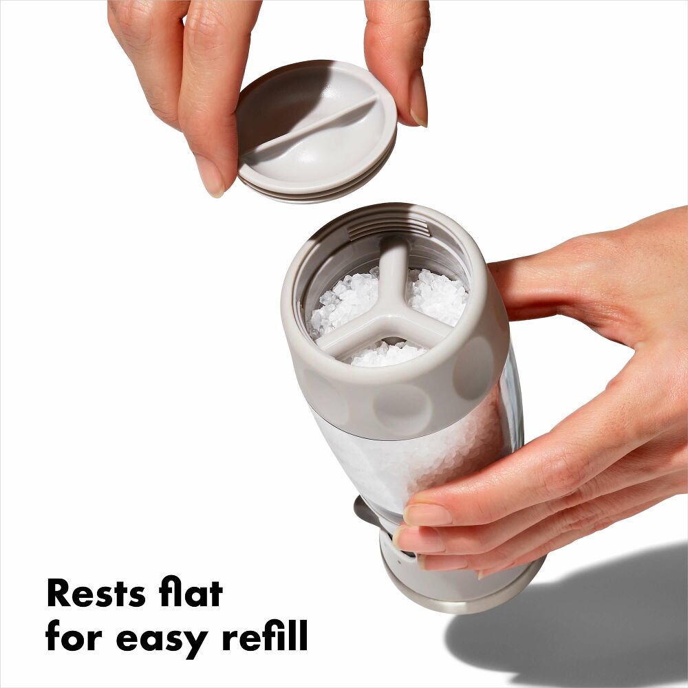 Hand holding salt grinder with rest flat salt refill. 
