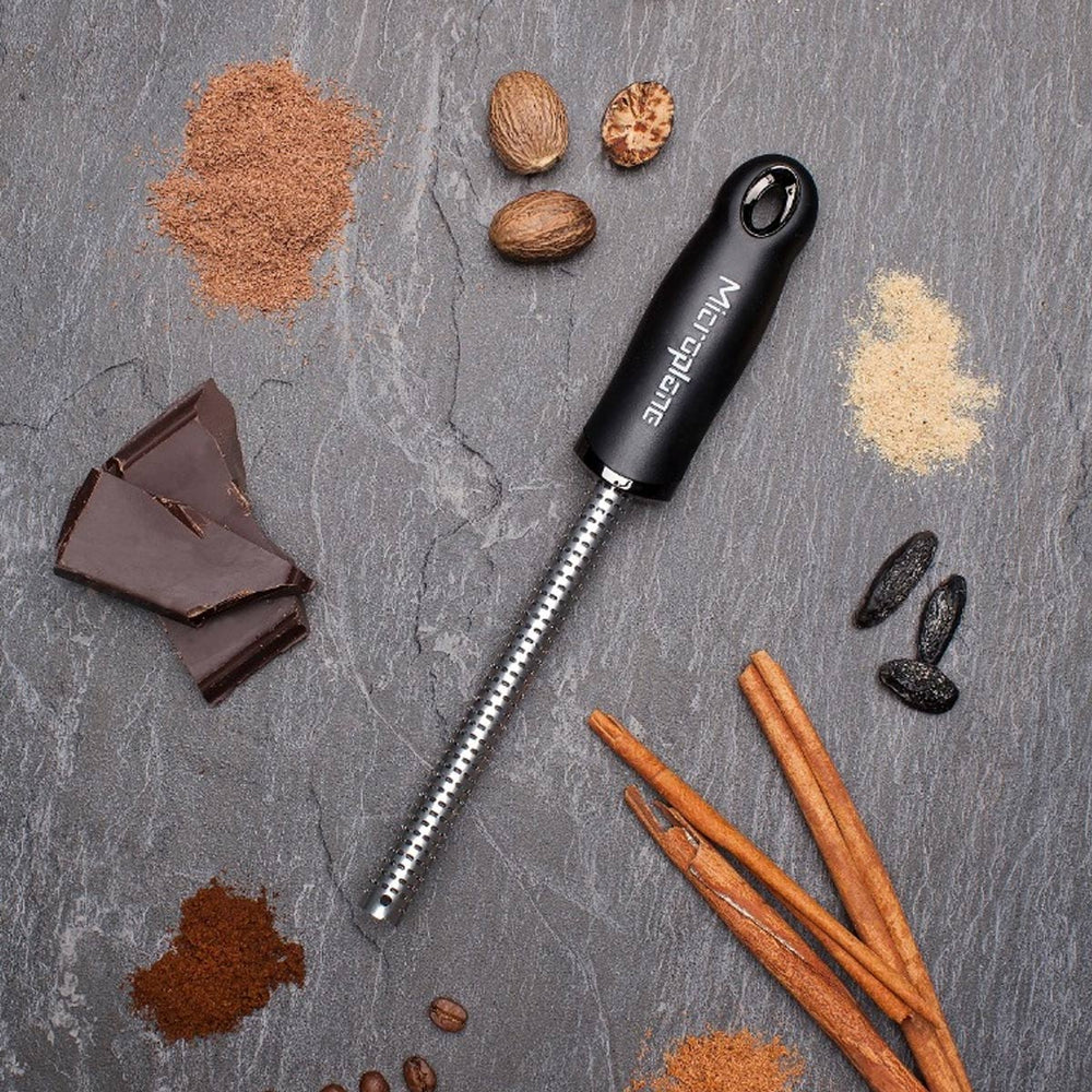 Spice grater on a grey slate surface with spices chocolate and nuts