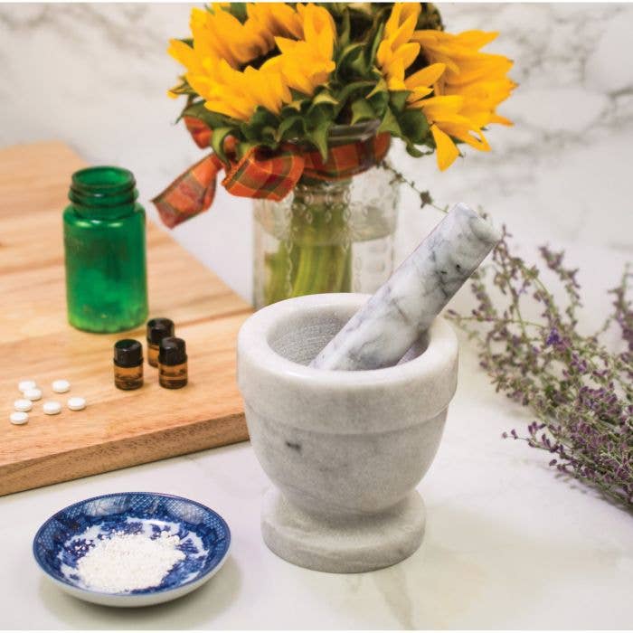 Mortar and pestle with a vase of sunflowers and bottles on a marble surface