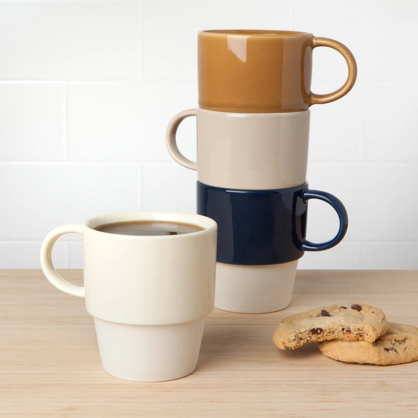 Three ceramic mugs stacked on a wooden surface with cookies.