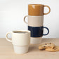 Three ceramic mugs stacked on a wooden surface with cookies.