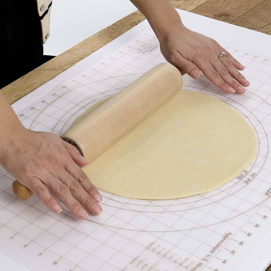 Person rolling out dough with a wooden rolling pin on a baking mat.