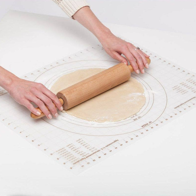 Person rolling out dough on a white surface with a wooden rolling pin