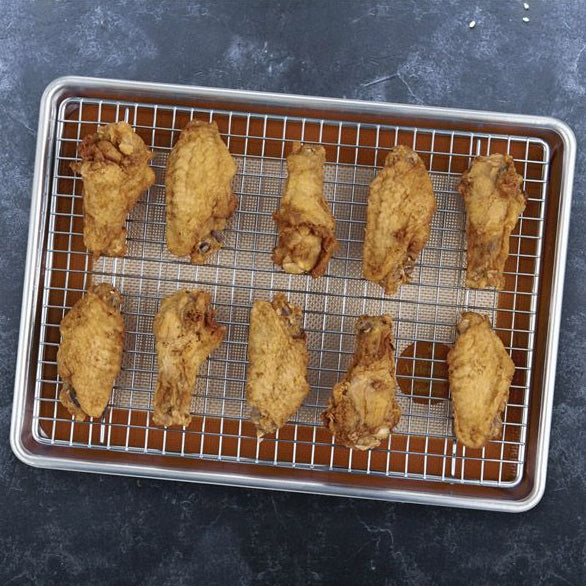 Baked chicken wings on a cooling rack and served with sauce on a black plate.