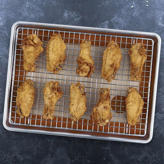 Baked chicken wings on a cooling rack and served with sauce on a black plate.